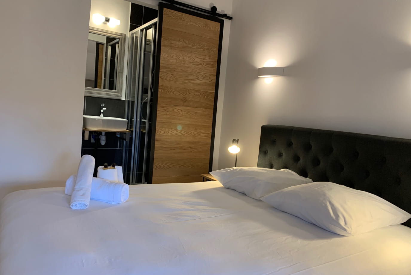 Lit capitonné avec porte coulissante en bois et salle de bain de la Chambre une personne à Ruoms à l'Hôtel Savel