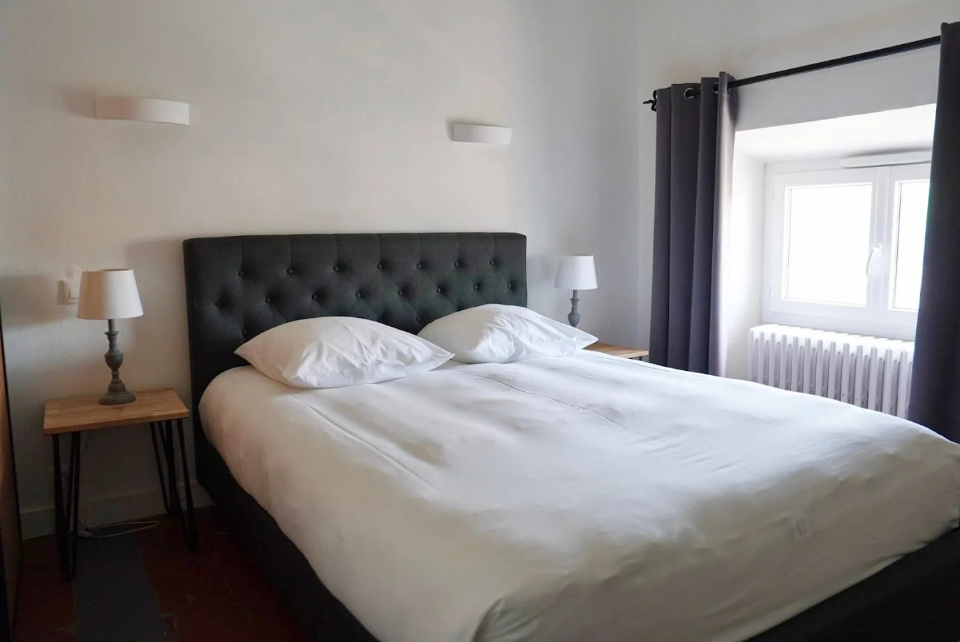 Lit capitonné sombre et fenêtre lumineuse de la Chambre Premium à l'Hôtel Savel de Ruoms en Ardèche