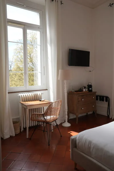 Chambre luxe climatisée avec sol en tomettes, chaise en rotin, commode ancienne et vue sur le jardin arboré, Hôtel Savel à Ruoms proche Vallon-Pont-d'Arc