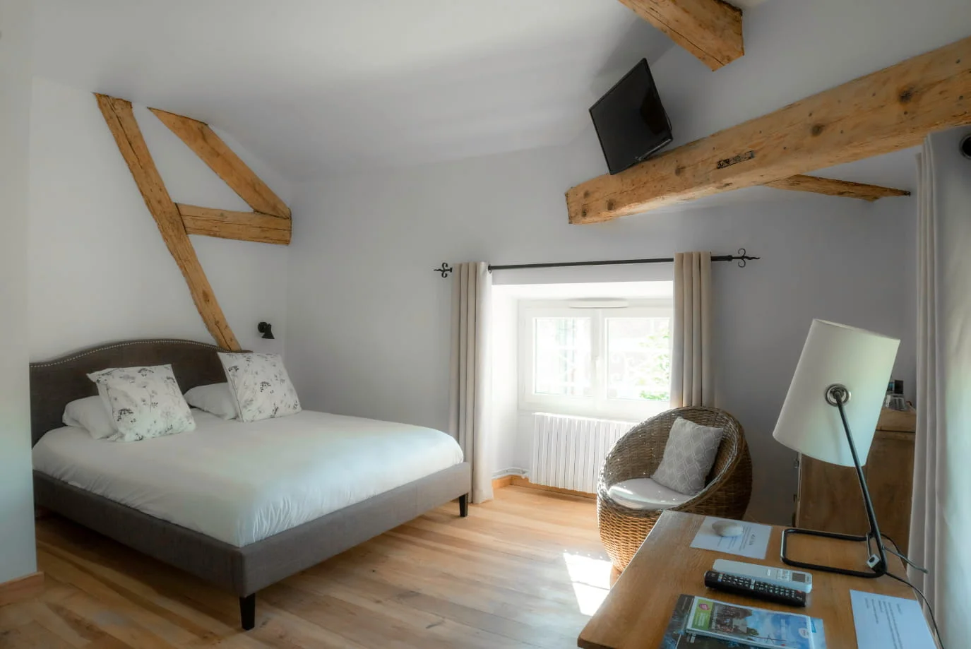 Overview of the Comfort Suite with exposed beams and rattan chair at Hotel Savel Ruoms, Ardèche
