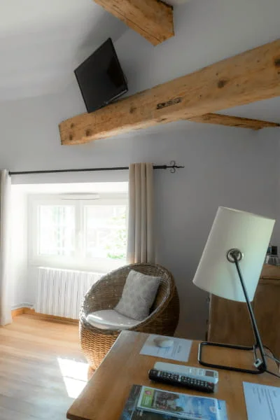 Coin bureau avec fauteuil en rotin et TV sur poutre apparente de la Suite Confort à l'Hôtel Savel Ruoms